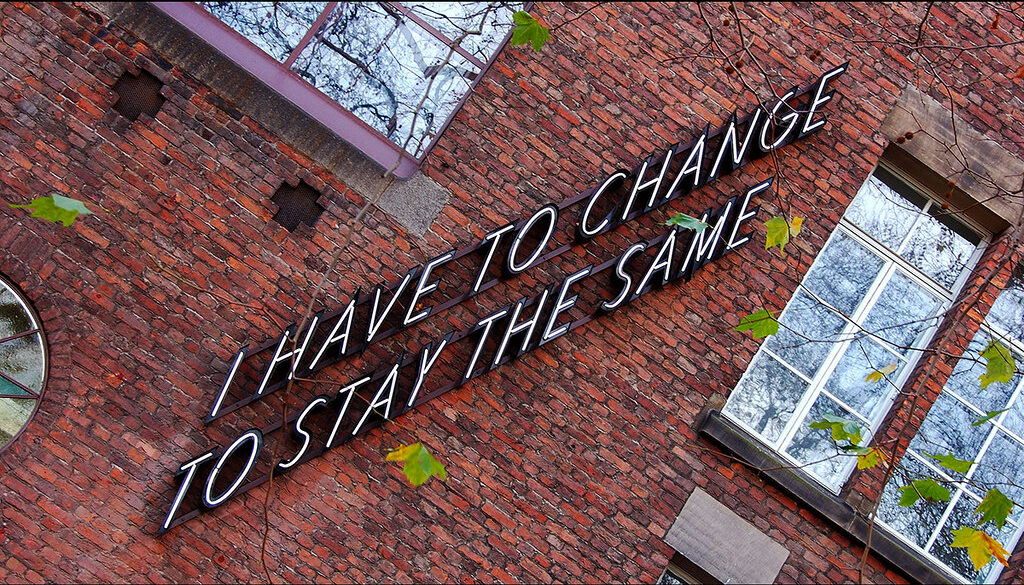 Gevel van de Willem de Kooning Academie met de neontekst "I have to change to stay the same"