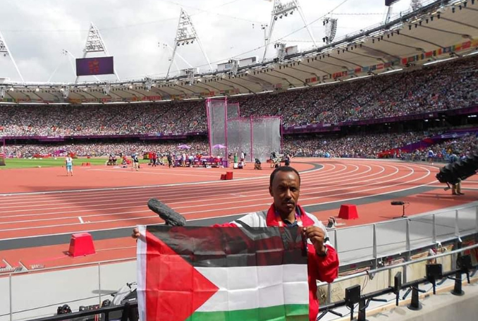 Abu Maharel, eerste Palestijnse Olympier, in een stadion met achter hem de renbaan. Hij spreidt een Palestijnse vlag 