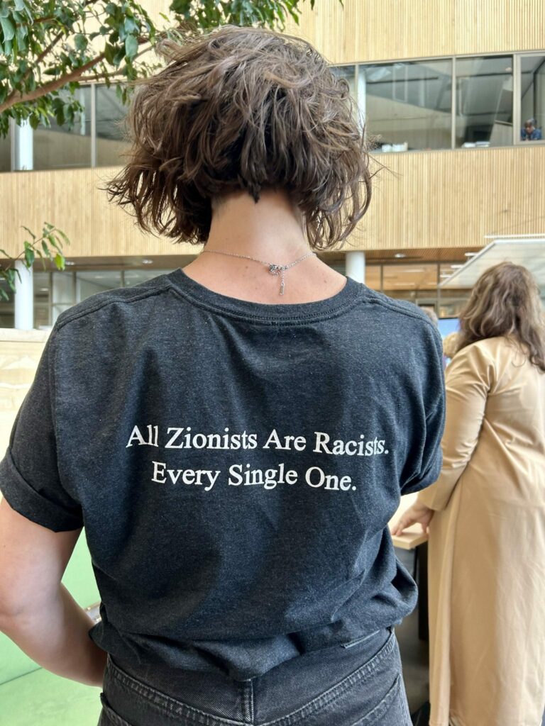 Kritische FNV-leden vroegen het hoofdbestuur om meer steun. Foto met donkerharig wit persoon met zwart t-shirt, op de rug gezien. Tekst op het shirt: All zionists are racists. Every single one.