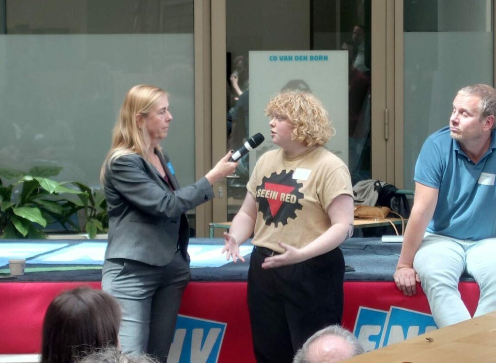 Kritische FNV-leden spraken met het hoofdbestuur over Palestina. Hier iemand in beige t-shirt met rode driehoek en host met grijs jasje. 