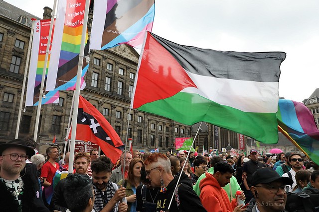 Pride Walk 2023 op de Dam, met Palestinavlag, Amsterdamvlag en Pride banners van de gemeente