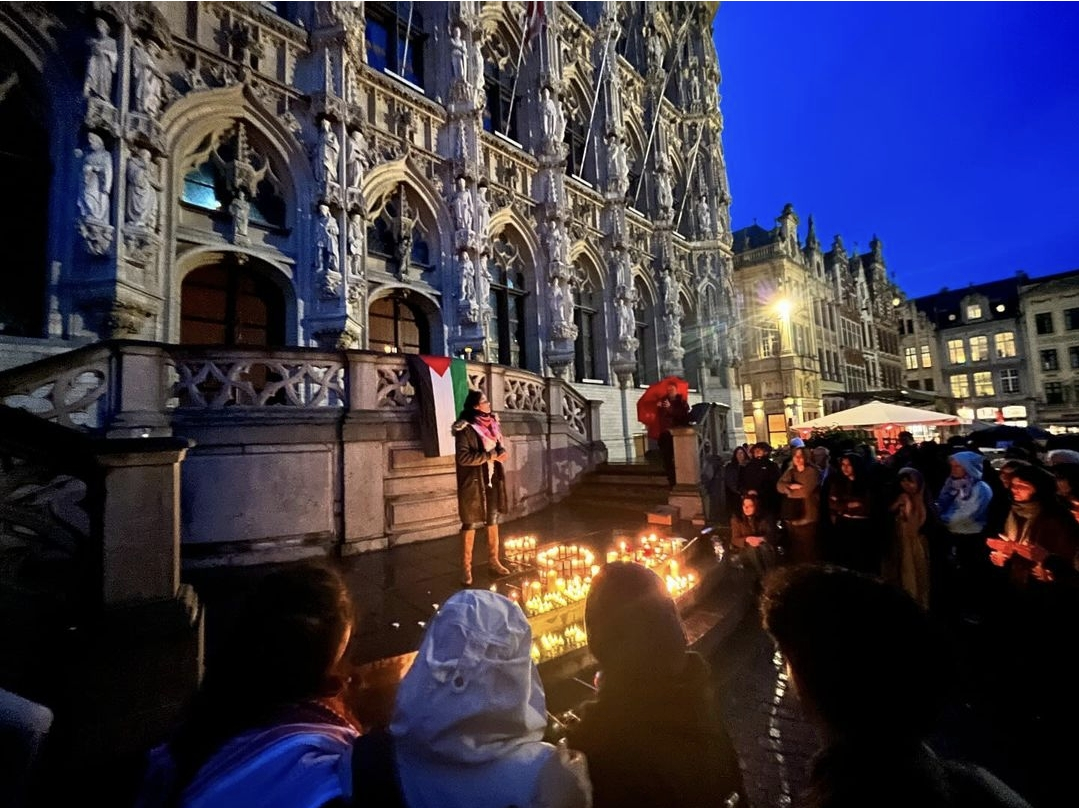 Wake voor Gaza vanwege een  jaar genocide. Op de Grote Markt in Leuven. Beeld van een groot oud gebouw in de avond, met veel kleine kaarsen en mensen