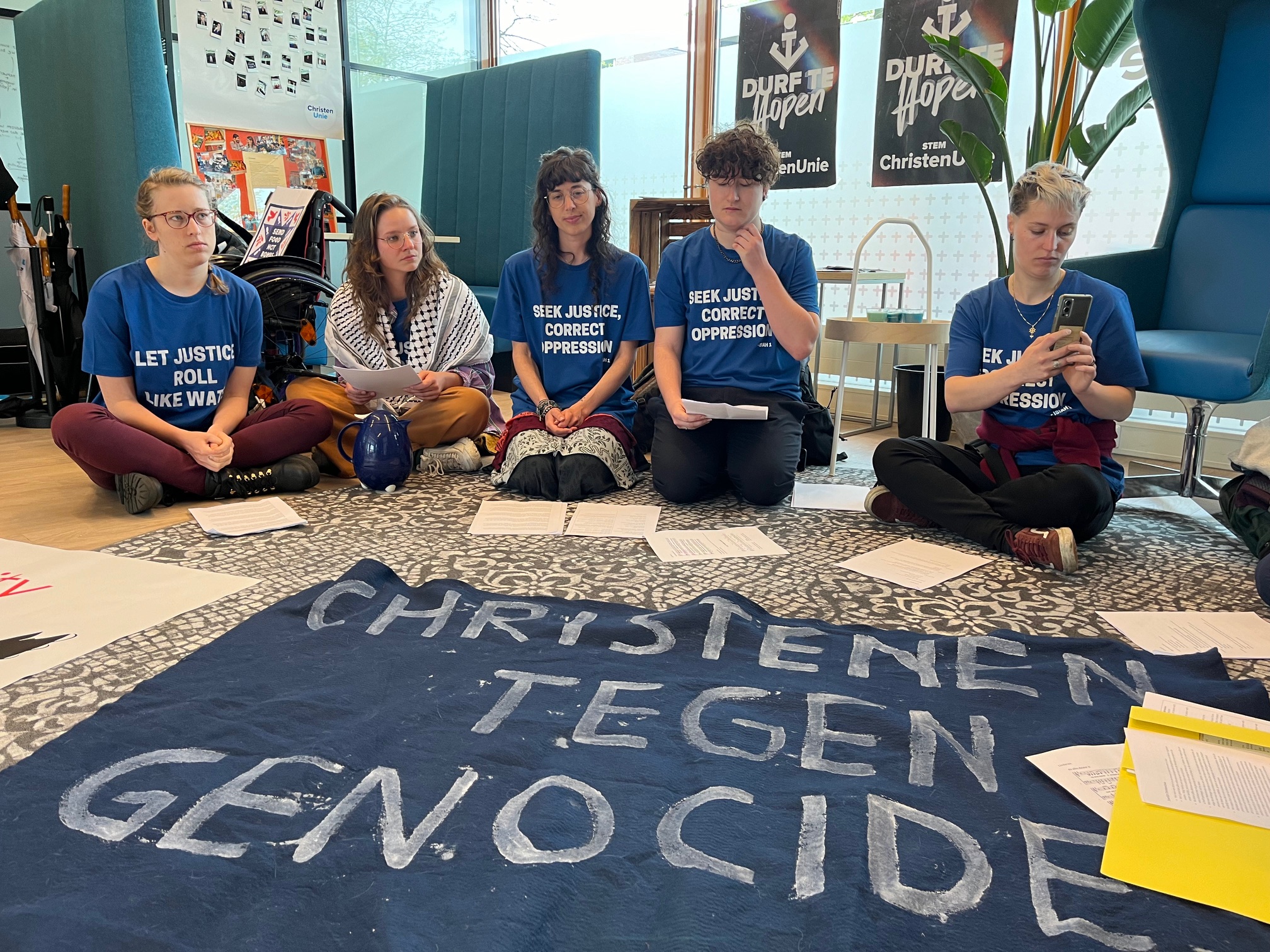 Bezetting van partijkantoor nChristenUnie door mensen van Christe;ijk COllecteif. Ze hebben een blauw t-shirt aan met opdruk waaronder "Let justice roll like water"