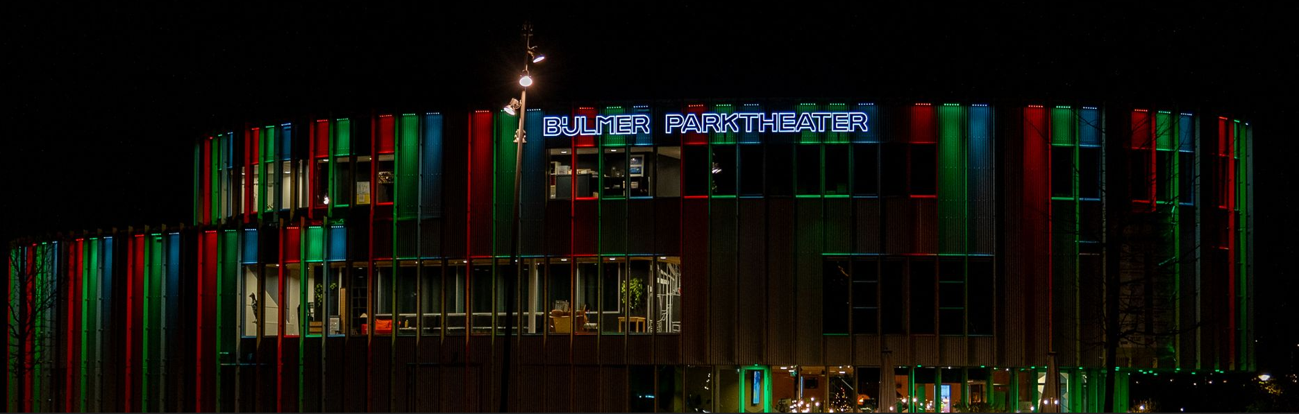 Foto van het Bijlmerparktheater met rode, groene en blauwe kleuraccenten op een donkere achtergrond